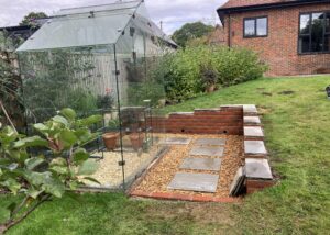 Completed brick retaining wall and landscaped gravel area around greenhouse in Winchester