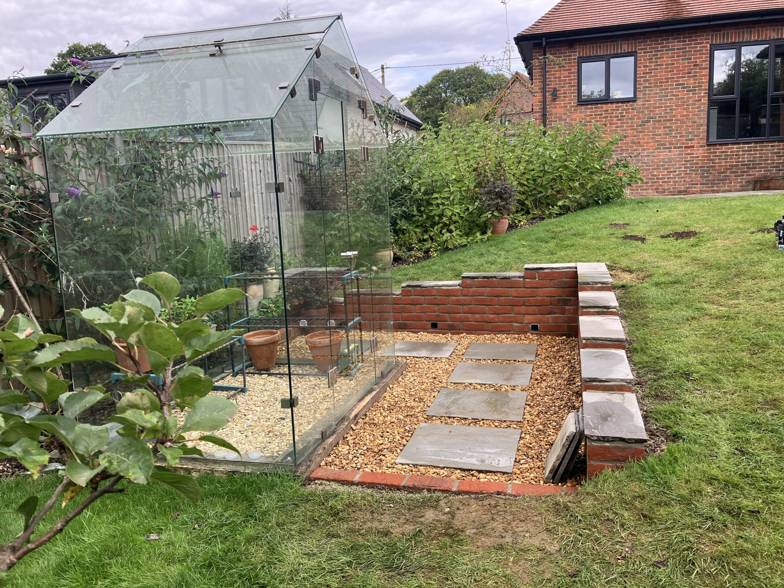 Completed brick retaining wall and landscaped gravel area around greenhouse in Winchester