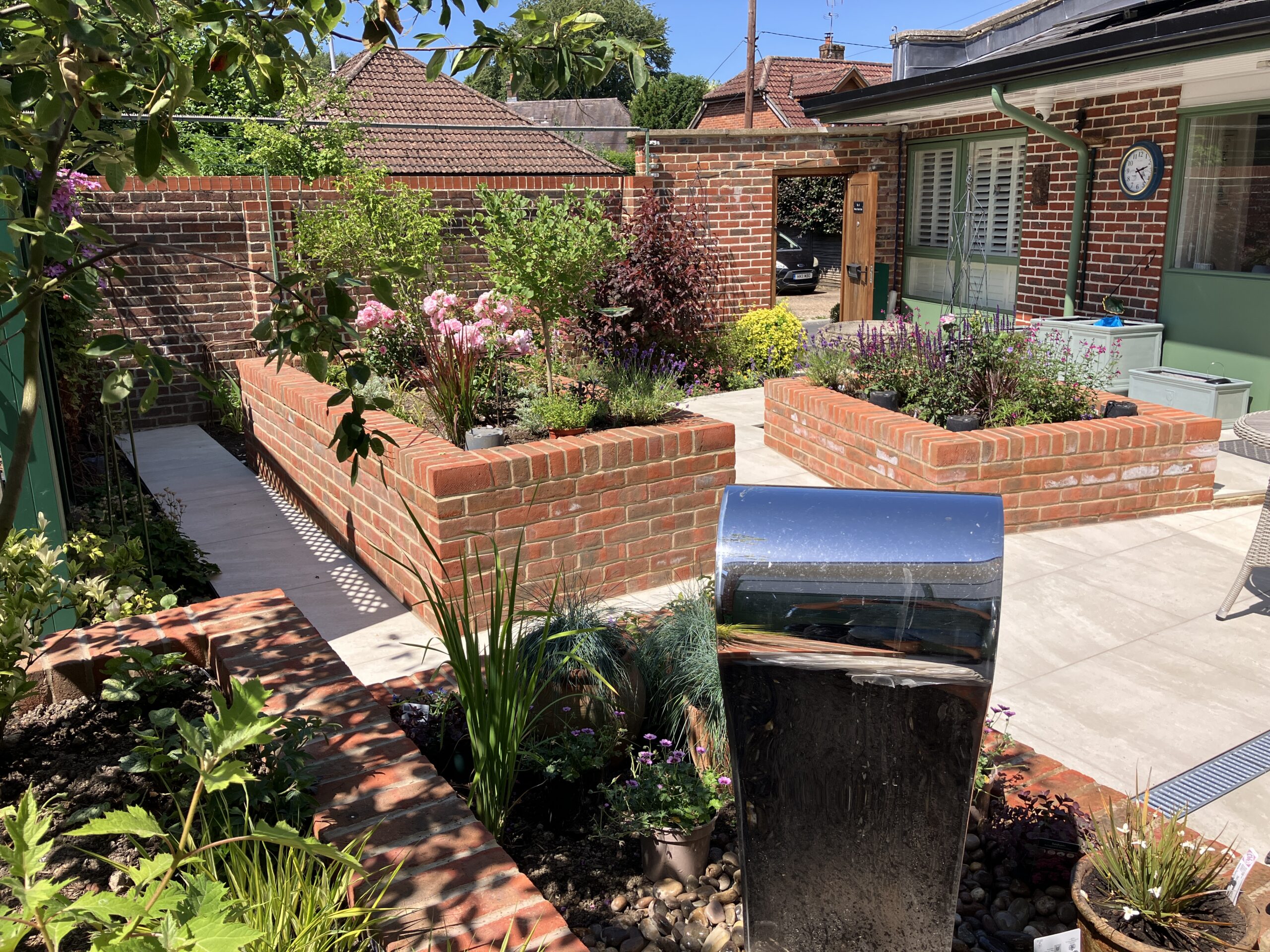 Raised red brick planting beds and beige porcelain patio in Winchester